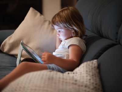 little child sitting comfortably in sofa watching tablet