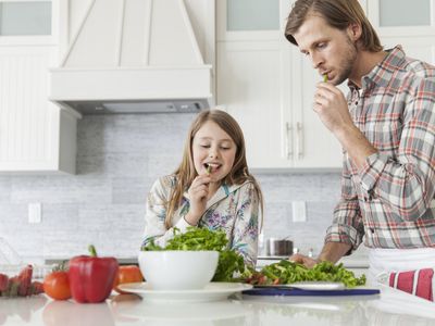 Father and daughter tasting food at kitchen island