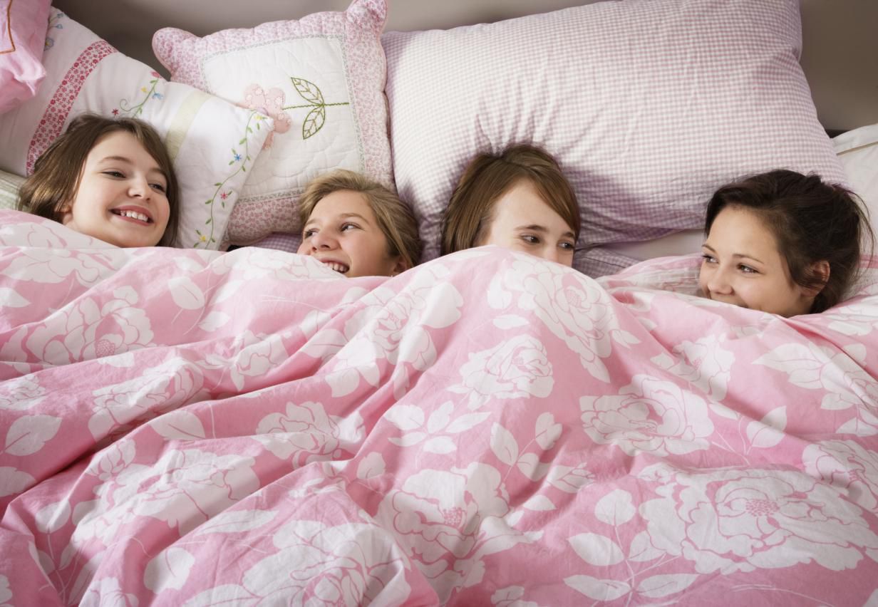 Four girls giggling in bed having a sleepover