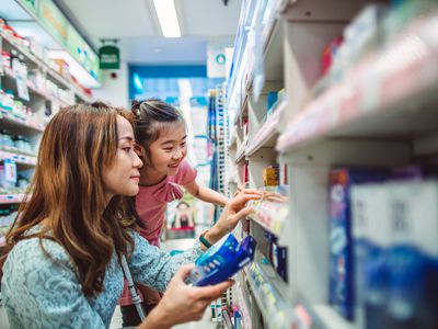 Asian woman and child crouching down at the drugstore examining medicine.