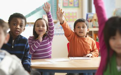 First grade classroom with children raising hands