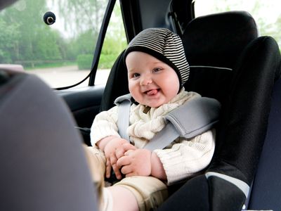 Baby wearing hat and sweater smiling in car seat.