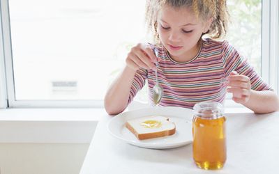 女孩(8-10)把蜂蜜涂在面包片上