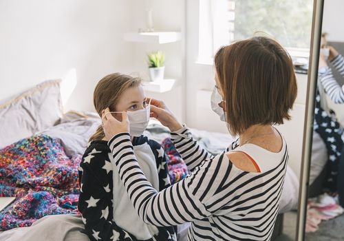 Mother putting face mask on her young daughter