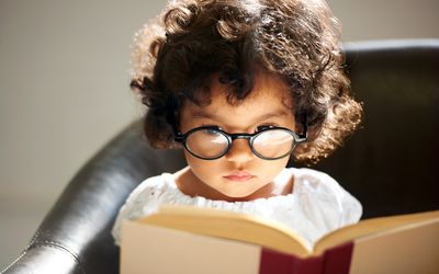 Little girl wearing glasses and reading a book