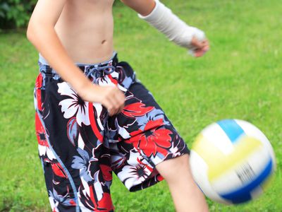 Boy wearing cast on arm kicking a soccer ball