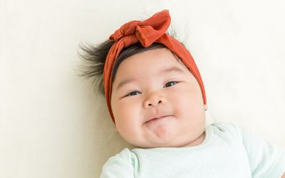 Baby girl with burnt orange headband and mint onesie looking at camera