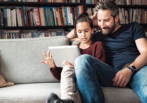快乐的父亲和女儿坐在沙发上看平板电脑