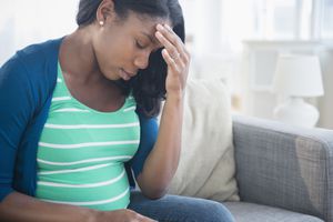 焦虑的黑人孕妇在沙发上揉额头＂width=
