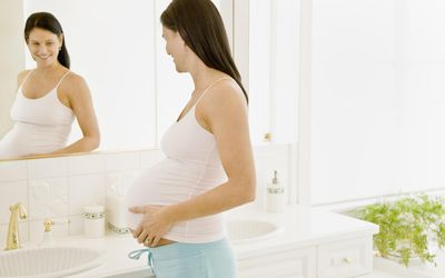 孕妇把手放在肚子上照镜子。