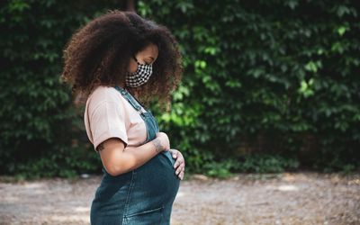 pregnant woman standing in a park holding her belly