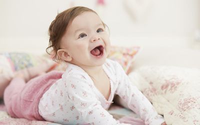 Smiling baby in pink pants with floral top pushing up from the ground