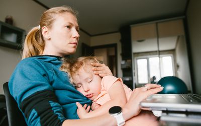 mother working with sleeping child in lap