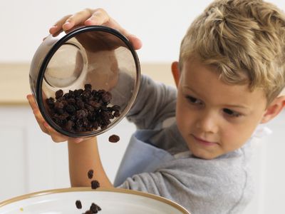 男孩pouring raisins into bowl of muesli mixture, 4 years