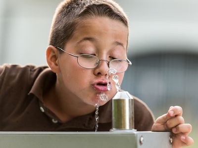 boy drinks water at school fountain.