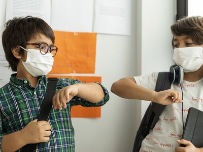 两个戴着口罩，拿着学习用品的学生撞肘。