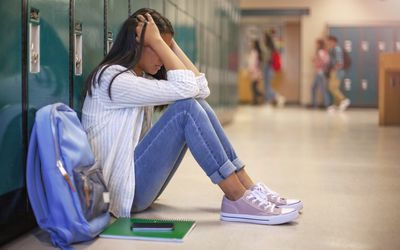 Side view of high school girl in illuminated corridor. She is against metallic lockers.