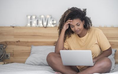 一个女人坐在床上看着电脑上的生育论坛