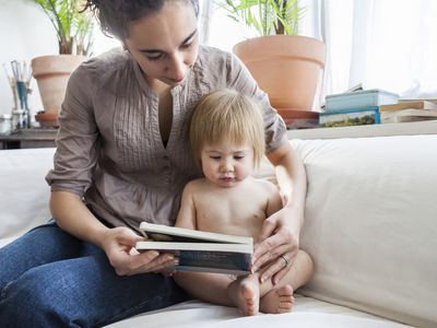 mother and baby sitting on couch together looking at a book