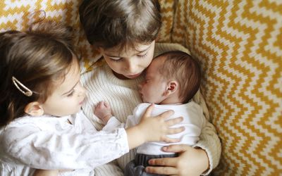 Two older siblings holding their new baby sibling