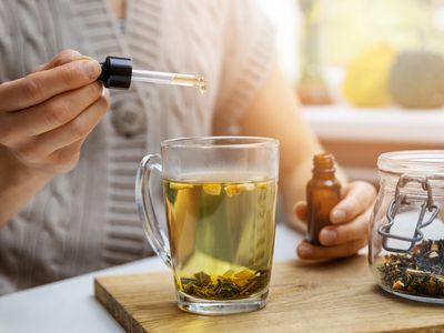 Woman dropping CBD oil into tea