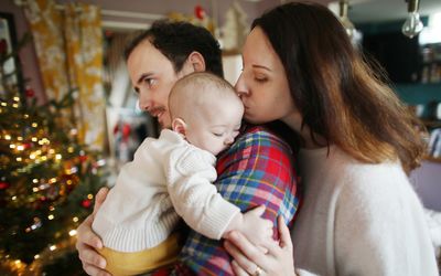 一个6个月大的婴儿在他的父母的怀里在家里，圣诞节的气氛