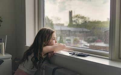 一个年轻的女孩在雨天望着窗外＂width=