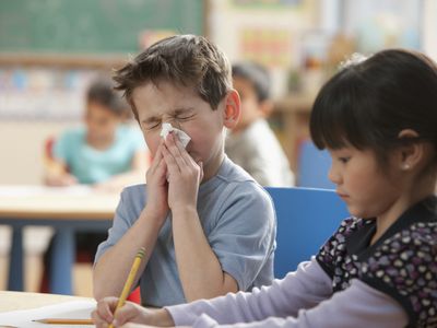 Caucasian boy blowing nose in classroom