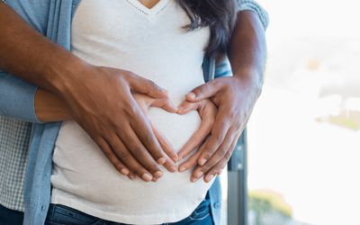 A couple with hands in a heart shape on the woman's pregnant belly