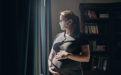 一位戴着口罩的孕妇望向窗外