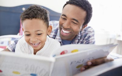 Happy father and son reading book together in bed