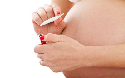 A pregnant woman holding a joint in front of her belly