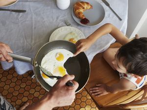 父母在早餐桌上为孩子提供煎锅煎蛋