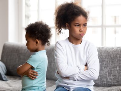 An angry brother and sister facing away from each other with arms crossed