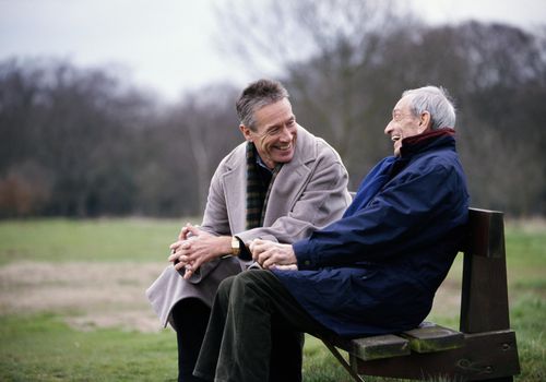 Elderly man laughing with his adult son on a park bench