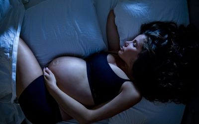 一个年轻的孕妇在半夜睡觉。舒适地依偎在枕头之间。
