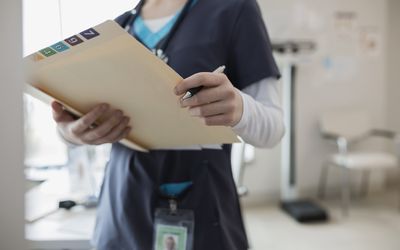 Nurse in scrubs holding medical chart in clinic