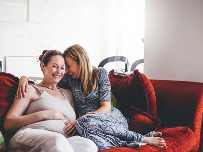 Mature lesbian couple, one parter is pregnant, sharing a laugh.