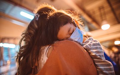 child wearing covid mask sleeping on mother's shoulder