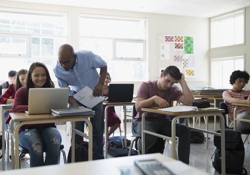 High school teacher helping student at laptop classroom