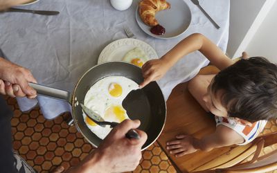父母在早餐桌上给孩子煎一锅煎好的鸡蛋