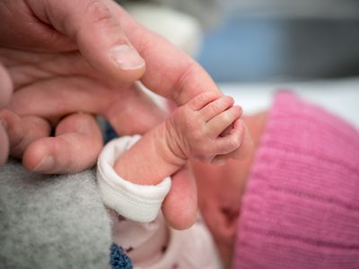 Premature newborn baby holding on to her grandfather's hand