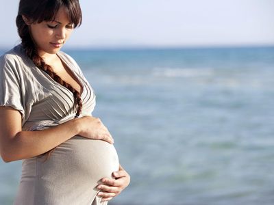 Pregnant woman holding her stomach on beach