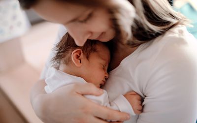 一个母亲抱着刚出生的儿子在家里的特写。年轻妇女满怀爱意地抱着她刚出生的男婴或女婴。