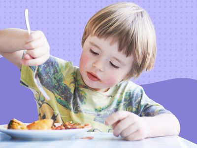 Child holding a fork over a plate of food displayed on a white surface against a purple patterned background
