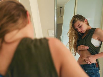 woman looking in mirror and pinching stomach