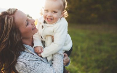 Portrait of mid adult woman carrying toddler daughter in field