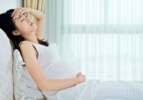 孕妇闭着眼睛摸着额头坐在床上