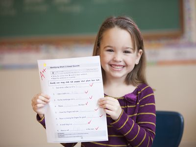 A smiling little girl holding a paper graded with an A++