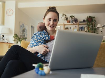 ther using laptop and holding her newborn baby at home